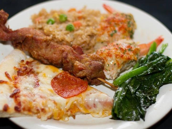 A plate with pizza, a beef skewer, fried rice and greens